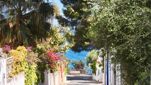 A narrow street flanked by white buildings with balconies, leading to a wooden bridge over a body of water. - Sea view apartment with FREE PARKING in the courtyard 30 meters from the sea on OFFER (Cala Gonone)