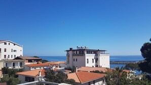 A coastal town with a prominent hotel named "Cataluna" featuring a modern design, terracotta roofs, and a view of the sea. - Sea view apartment with FREE PARKING in the courtyard 30 meters from the sea on OFFER (Cala Gonone)