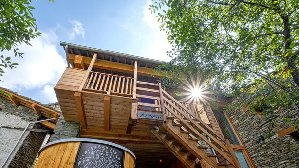 A wooden building with a balcony and a staircase leading to a second level. - Amelù (Ostana)