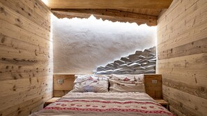 A wooden cabin-style room with a bed, pillows, and a unique mountain-patterned headboard. - Amelù (Ostana)