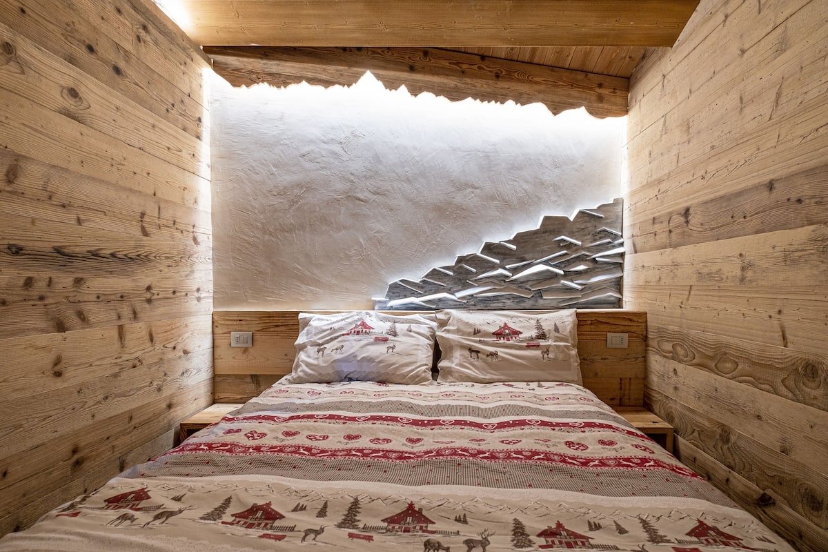 A wooden cabin-style room with a bed, pillows, and a unique mountain-patterned headboard.