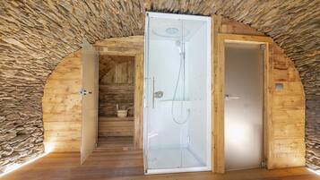 A wooden interior with a stone ceiling, a glass-enclosed shower, and a wooden door.
