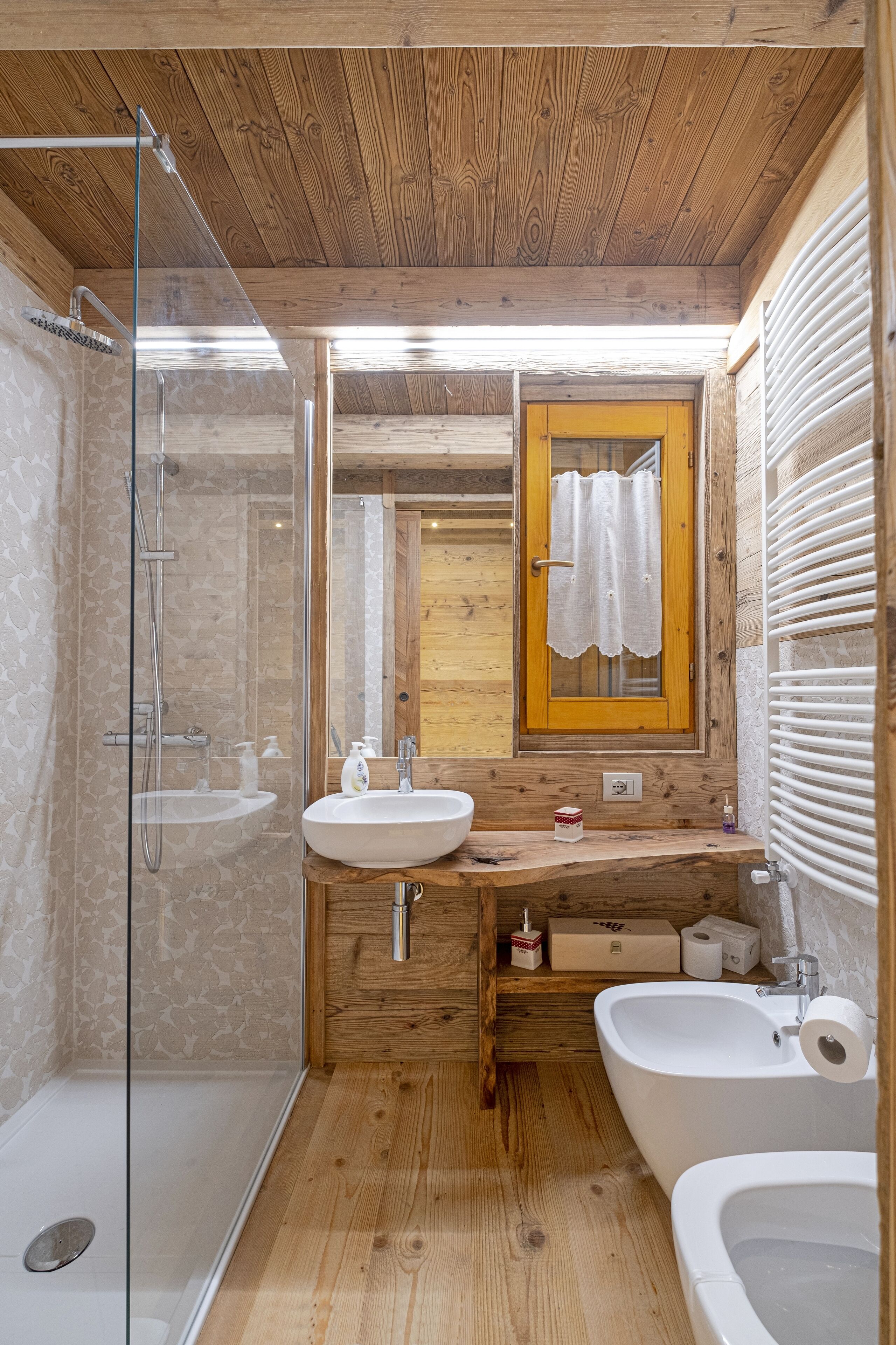 Un baño con paneles de madera, ducha envuelta en vidrio, lavamanos, lavadero y retrete.