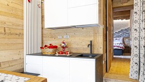 A compact kitchen with wooden walls, a white countertop, and a small stool. - Amelù (Ostana)