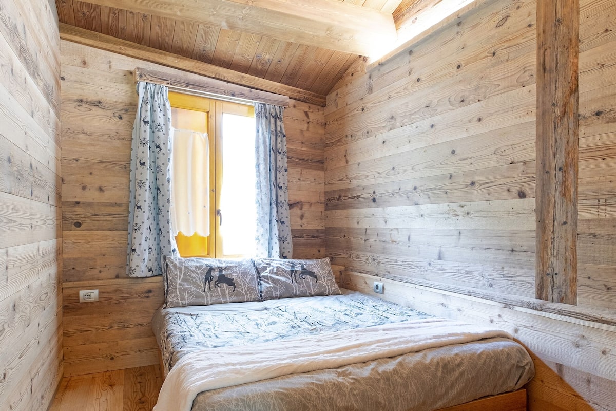 A wooden cabin bedroom with a bed, curtains, and a window.