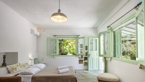 Ein Schlafzimmer mit einem Bett, einem Sessel, einem kleinen Hocker und einem Fenster mit grünen Rollläden.