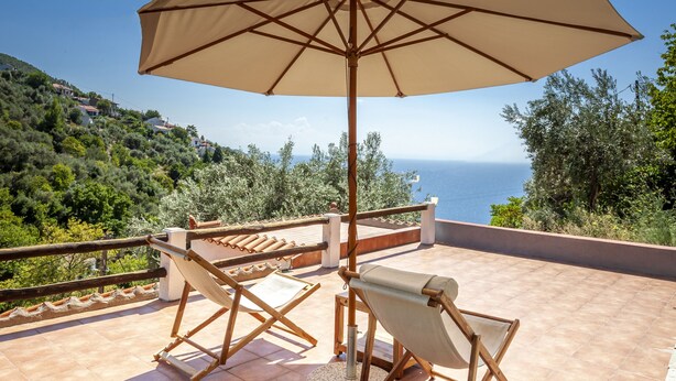 Eine Terrasse mit Tisch und Stühlen, einem Sonnenschirm und Blick aufs Meer.