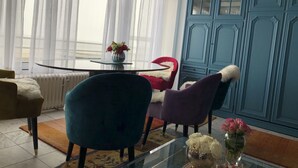 A dining area with a round glass table, two chairs, a vase with flowers, and a blue cabinet.