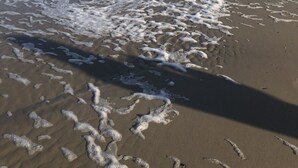A beach with waves and footprints in the sand.
