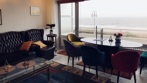 A living room with a leather sofa, a glass coffee table, and a view of the ocean through large windows.