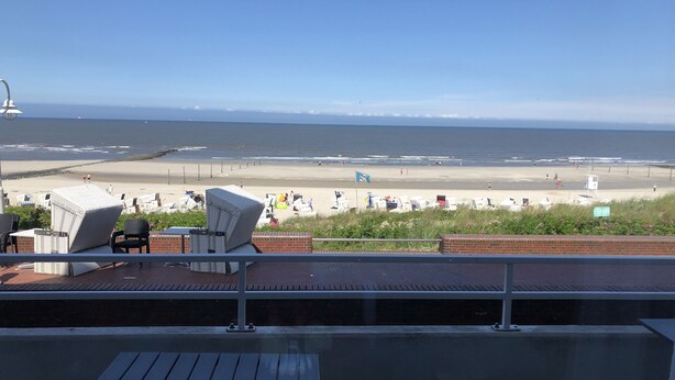 A balcony with a view of a beach and ocean. There are lounge chairs and a table on the balcony.