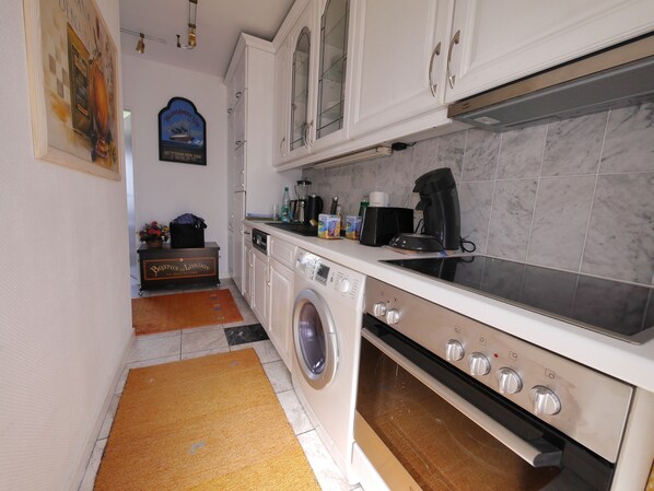 A compact kitchen with white cabinets, a built-in washing machine, and a stove.