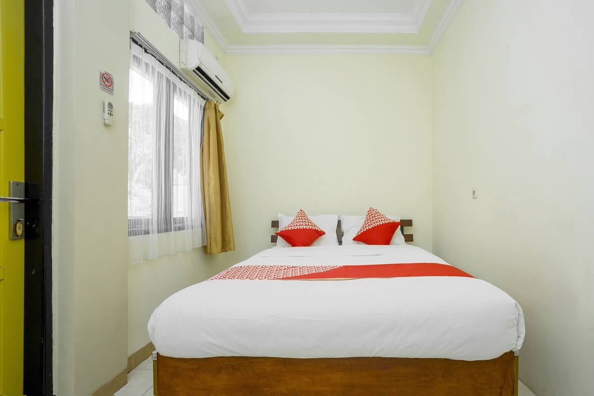 A hotel room with a bed, curtains, and an air conditioning unit.