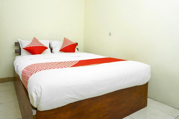 A neatly made bed with a wooden frame, white bedding, and red and white patterned pillows.
