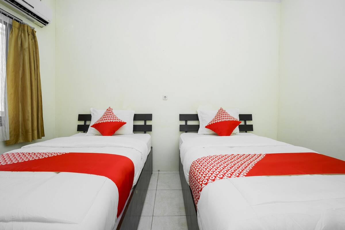 A hotel room with two beds, each with a red and white patterned bedspread and matching pillows.