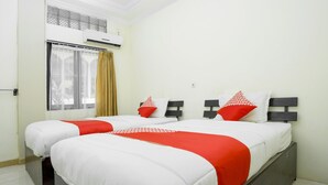 Uma cama de casal com roupa de cama branca e vermelha, uma janela com cortinas e um aparelho de ar condicionado.