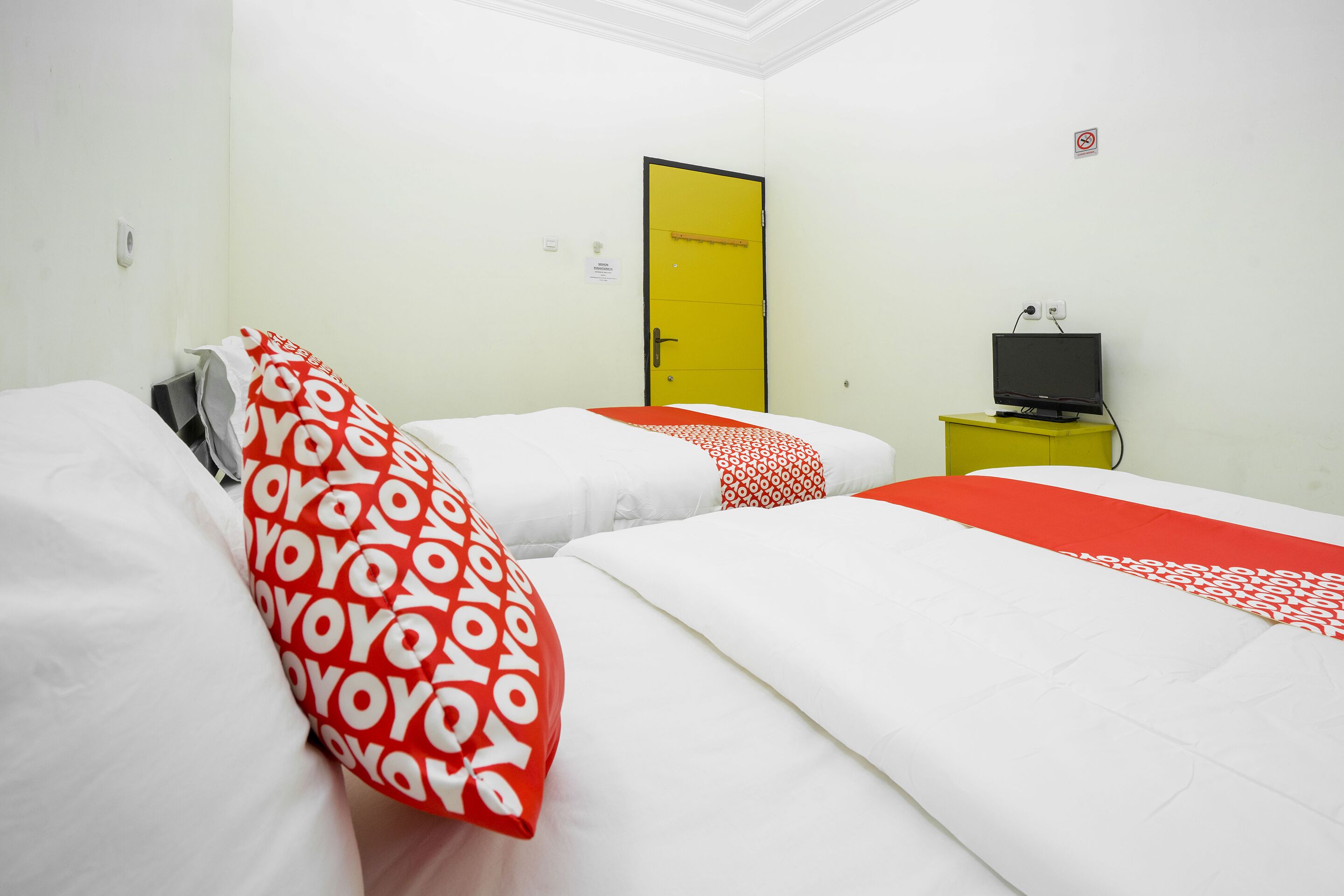 A hotel room with two beds, a yellow door, a television on a yellow stand, and a sign on the wall.