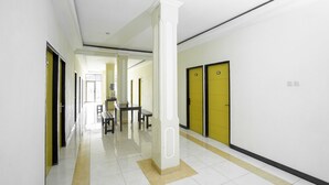 Um corredor com paredes brancas, portas amarelas e um pilar central.