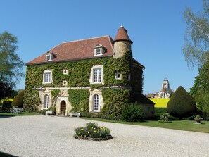 A historic building with ivy-covered walls, a turret, and a gravel driveway.