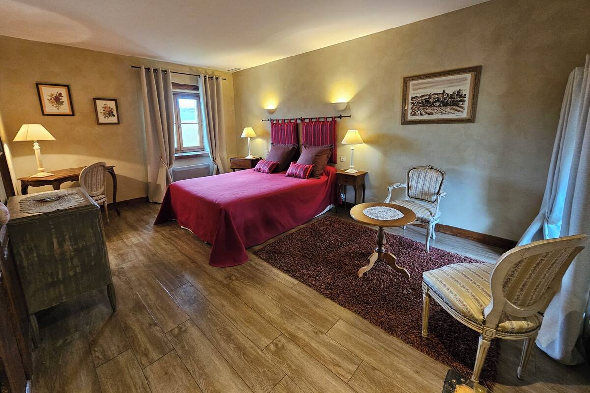 A hotel room with a bed, two bedside tables, a chair, a small round table, and a window with curtains.