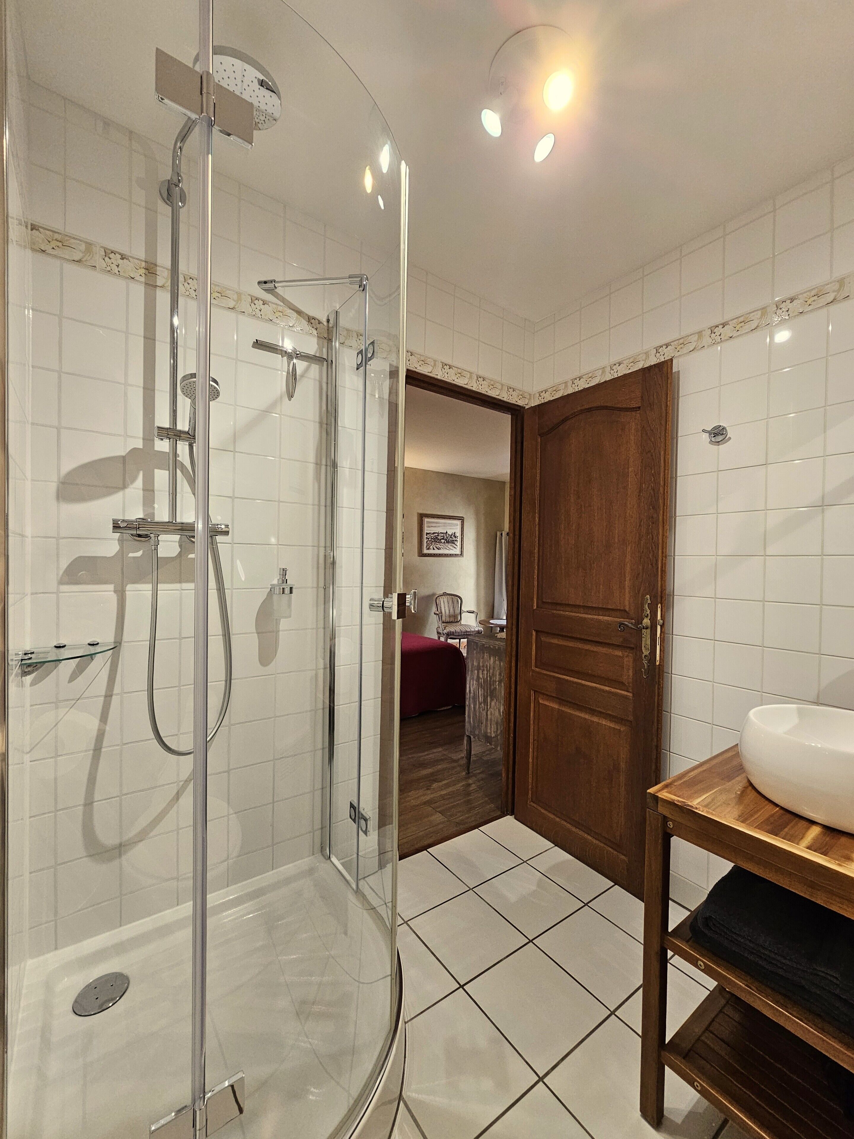 Ein Badezimmer mit einer Duschkabine aus Glas, einer Holztür und einem Waschbecken mit einer Holzablage.