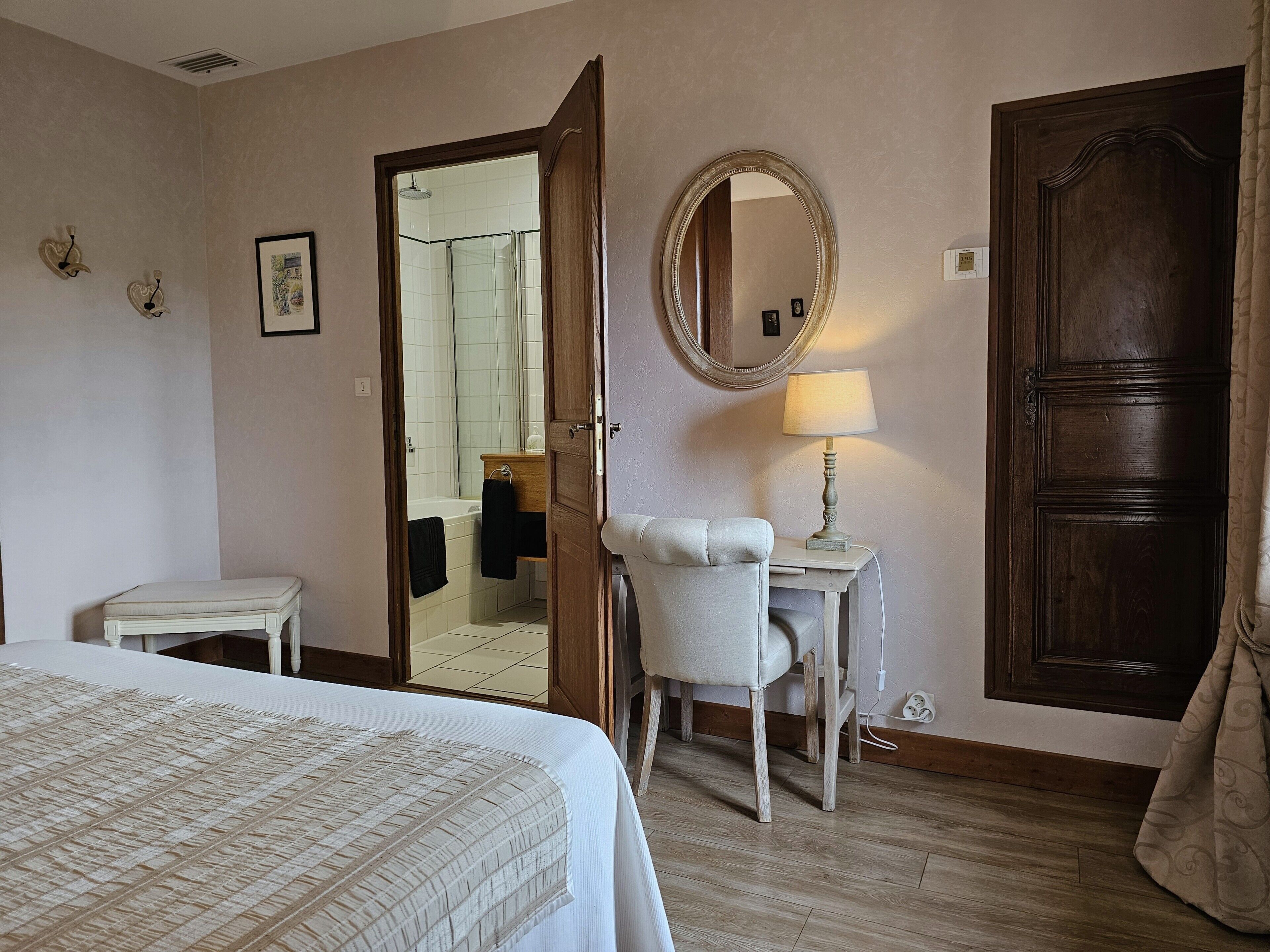 A hotel room with a bed, a desk with a chair, a mirror, and a door.