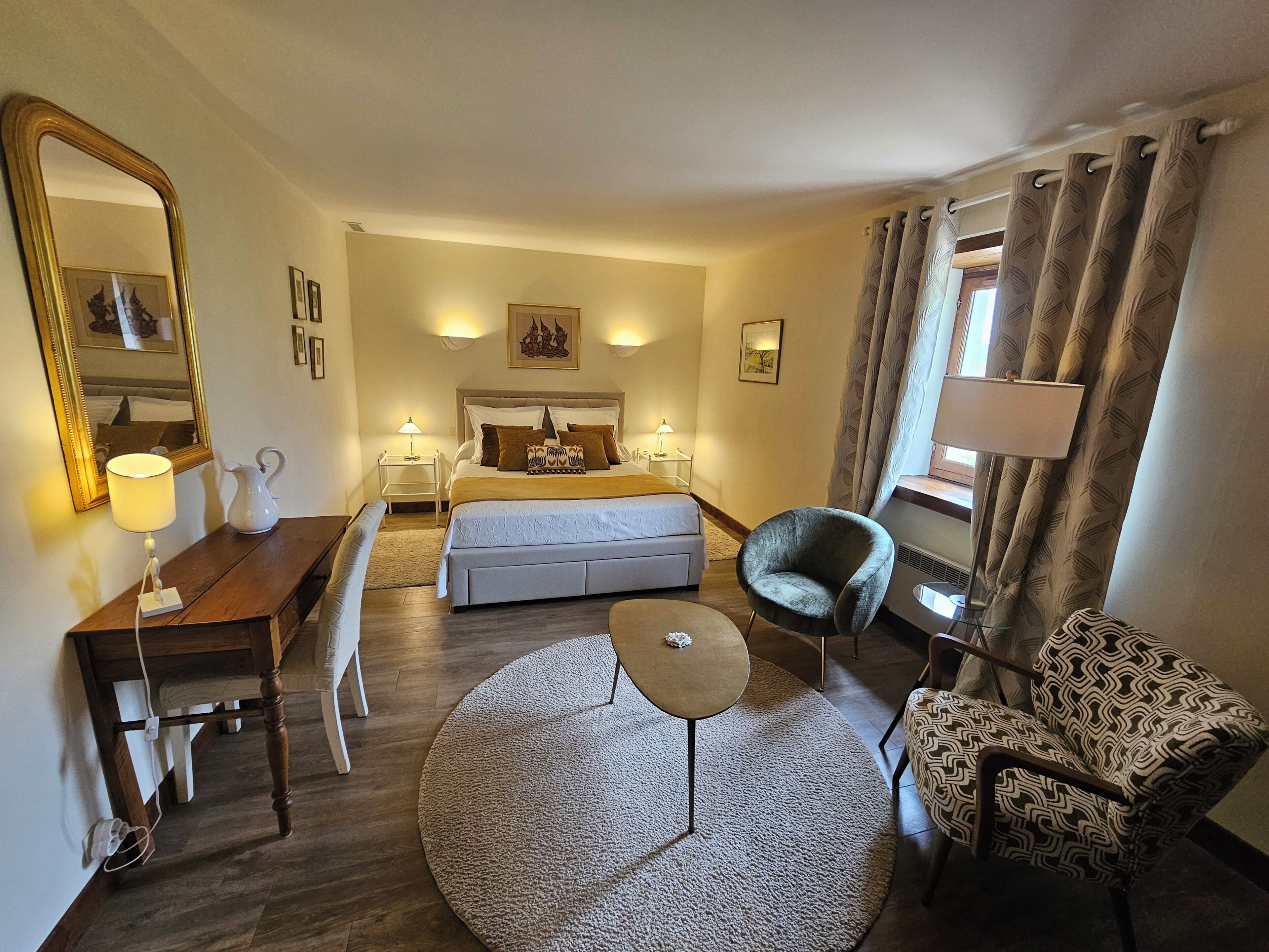 A hotel room with a bed, bedside tables, a desk, a chair, a round rug, and a large mirror.