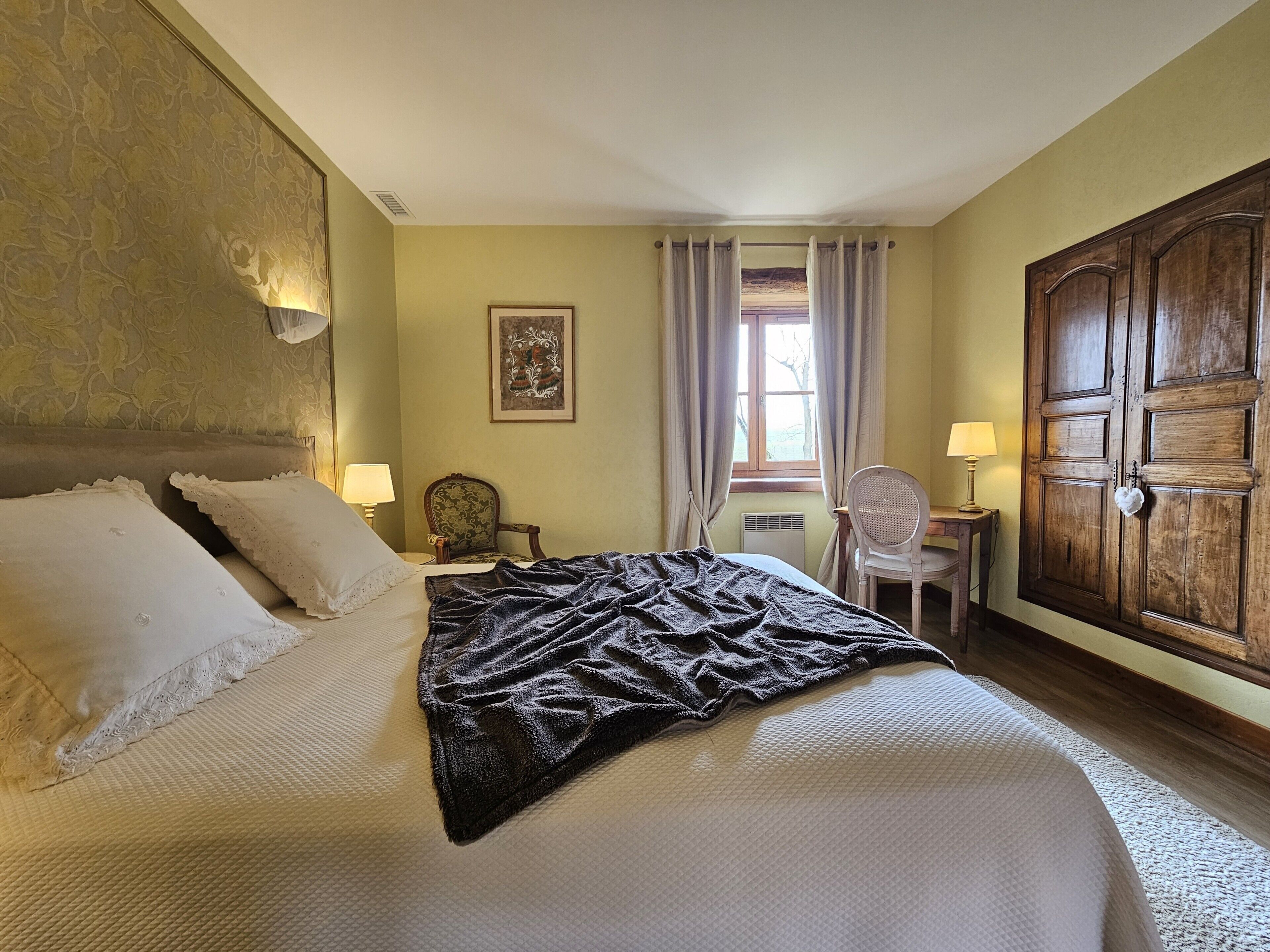 A hotel room with a large bed, a desk, a chair, and a wardrobe.