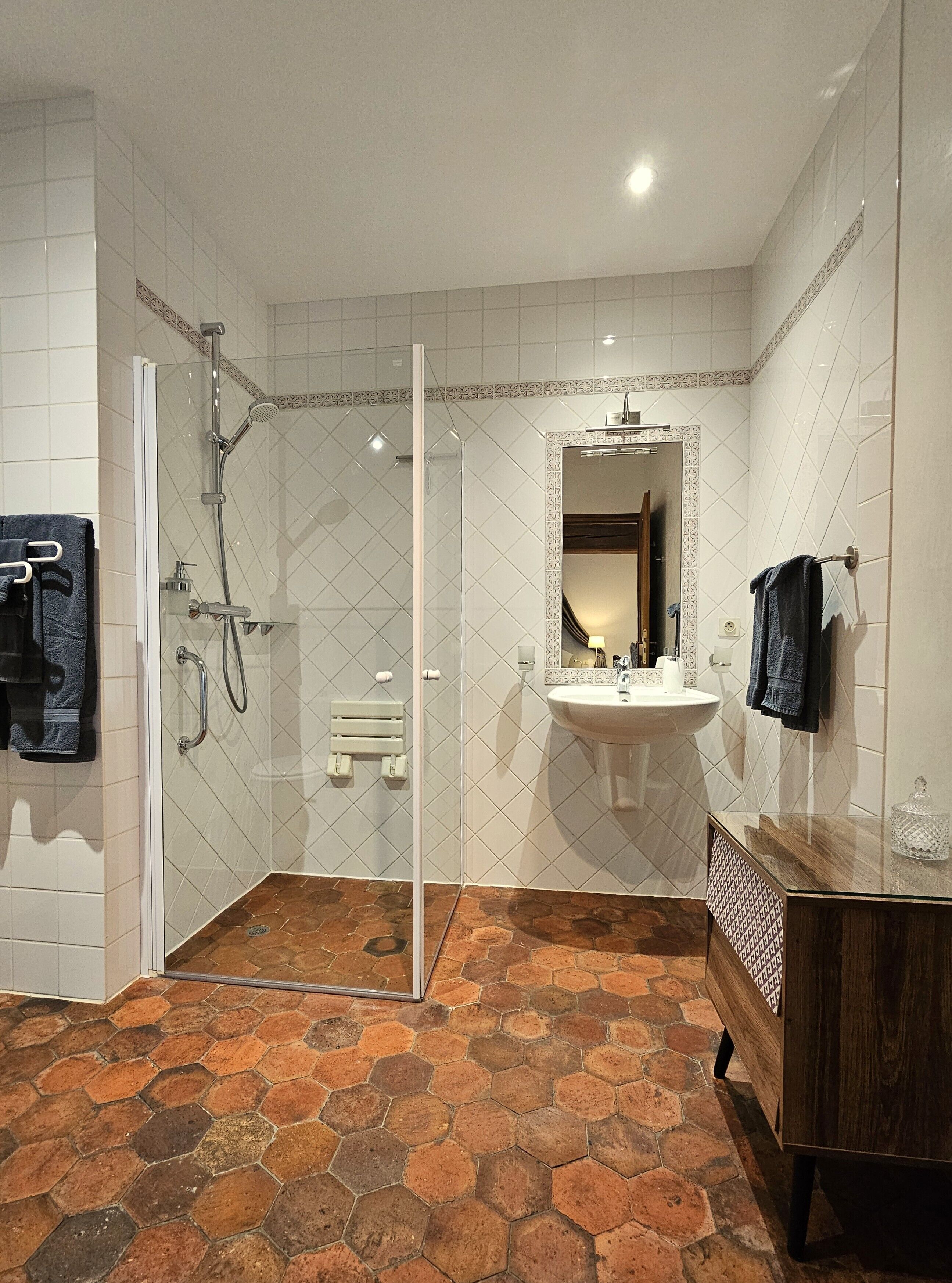 A bathroom with a glass-enclosed shower, a sink with a mirror, and a wooden vanity.