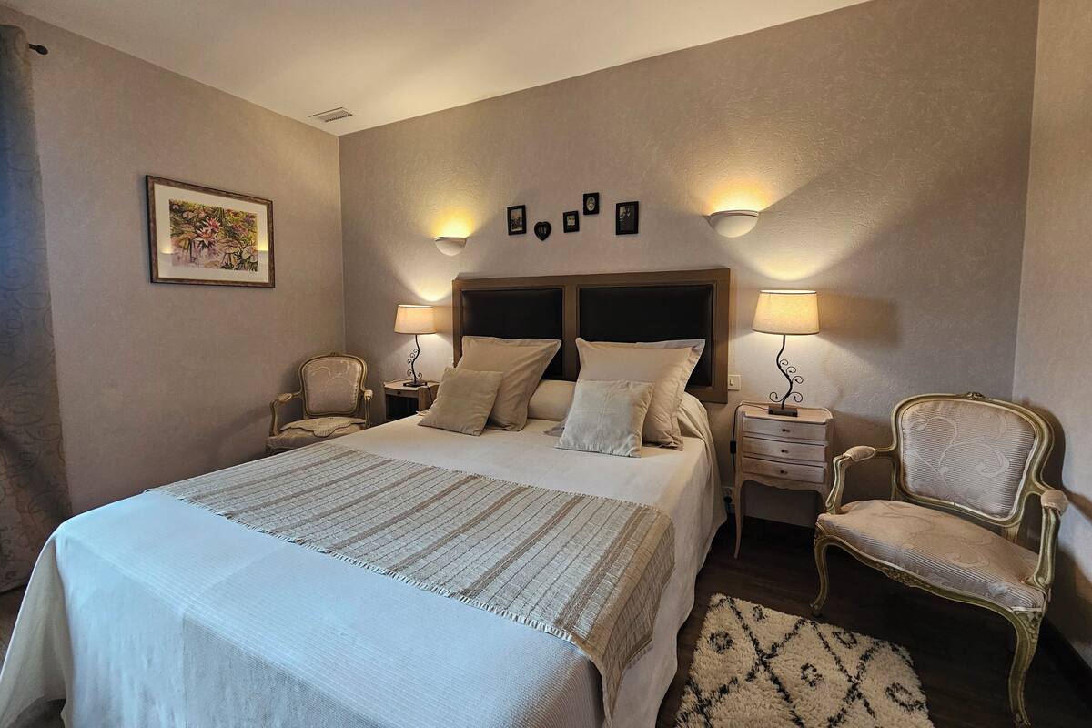 A bedroom with a large bed, two bedside tables, a chair, and wall-mounted lamps.