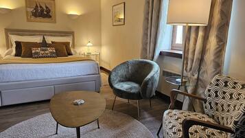 A hotel room with a bed, a chair, a small table, a lamp, and curtains.