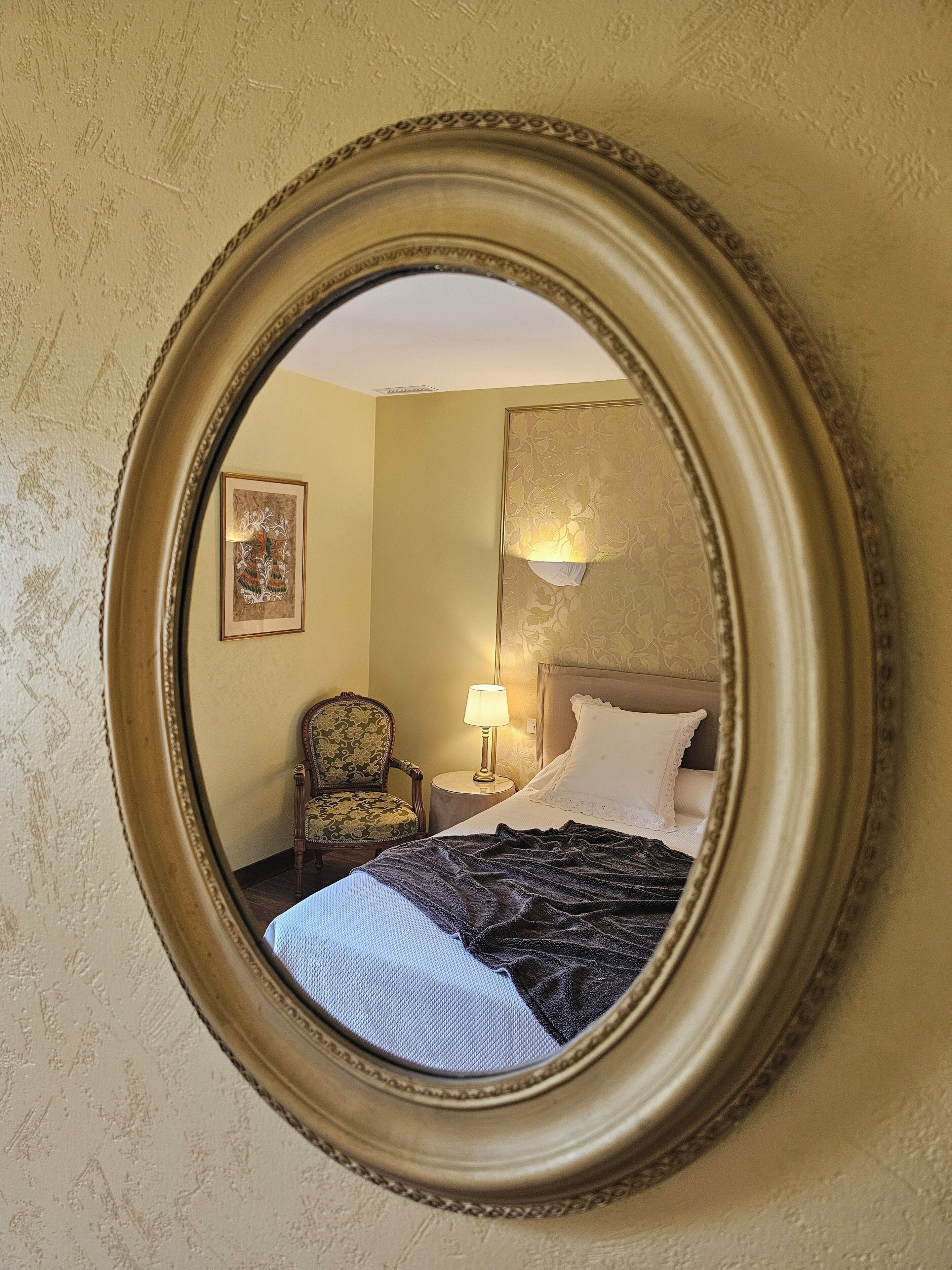 Een kamer met een bed, een stoel, een lamp en een ingelijst schilderij aan de muur.