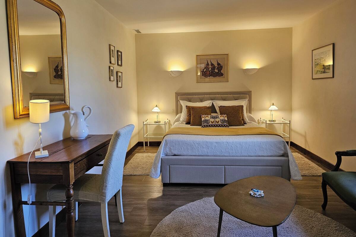A hotel room with a bed, bedside tables, a desk, a chair, a coffee table, and a large mirror.