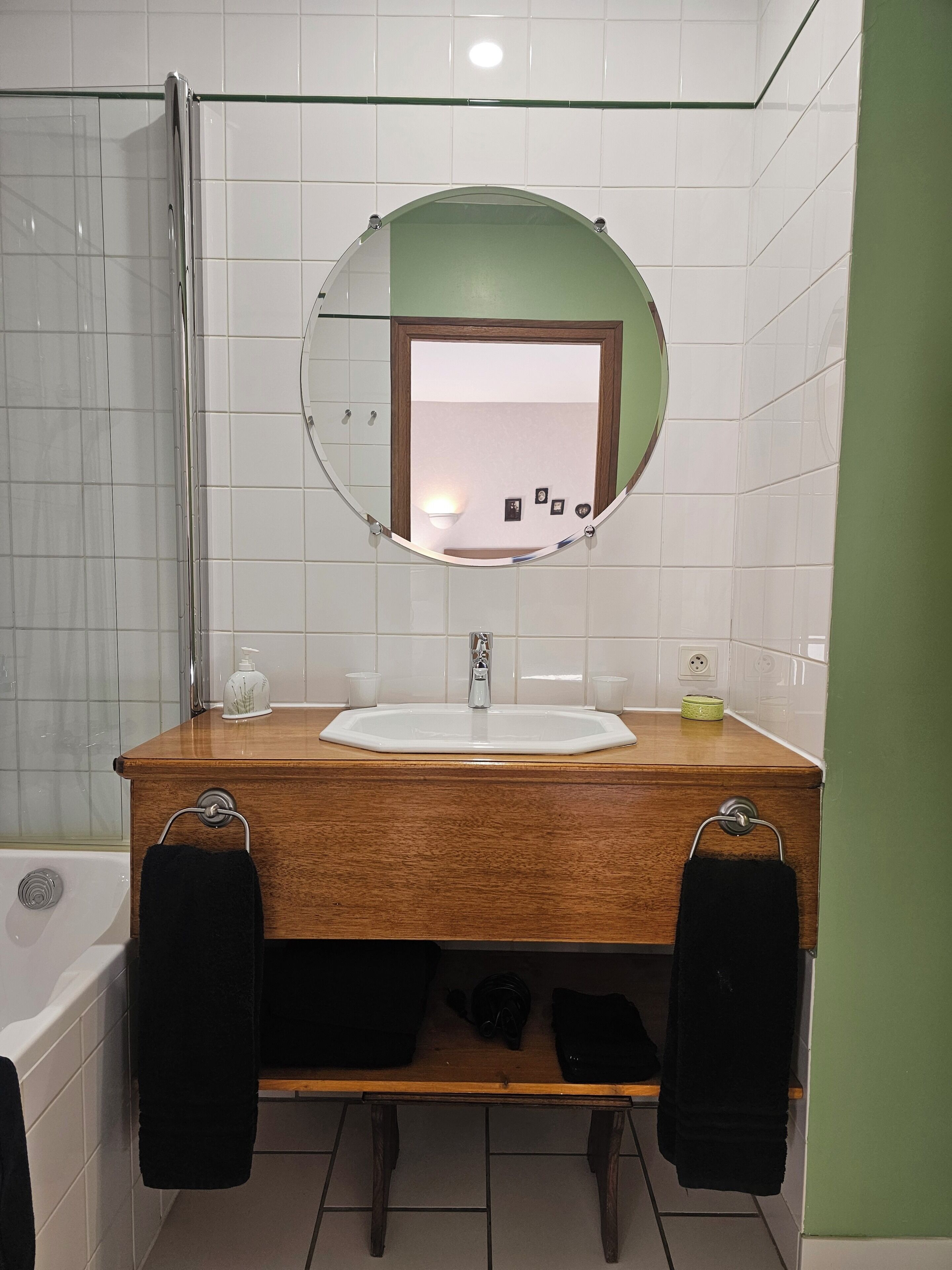 Een badkamer met een houten wastafel, een ronde spiegel, een witte wasbak en een douchehoek.