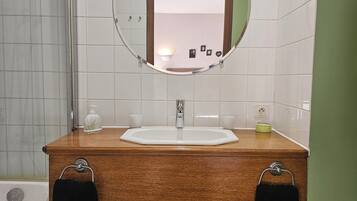 A bathroom with a wooden vanity, a round mirror, a white sink, and a shower area.