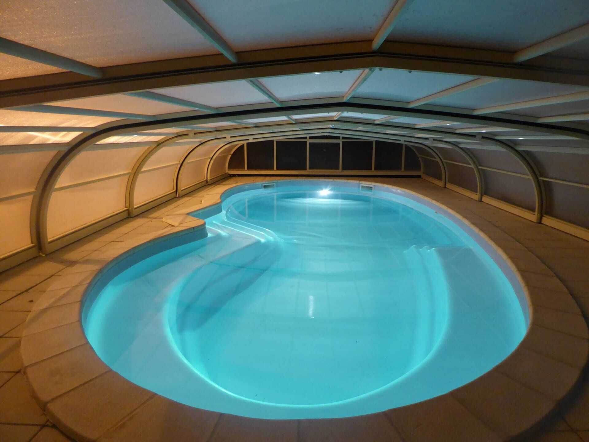 Une piscine intérieure au design incurvé, entourée d’un sol carrelé et surmontée d’une structure de plafond également incurvée.