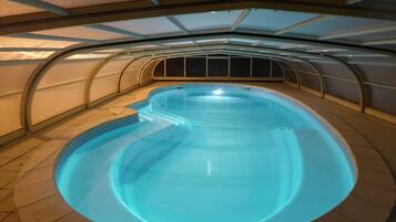 Une piscine intérieure au design incurvé, entourée d’un sol carrelé et surmontée d’une structure de plafond également incurvée.