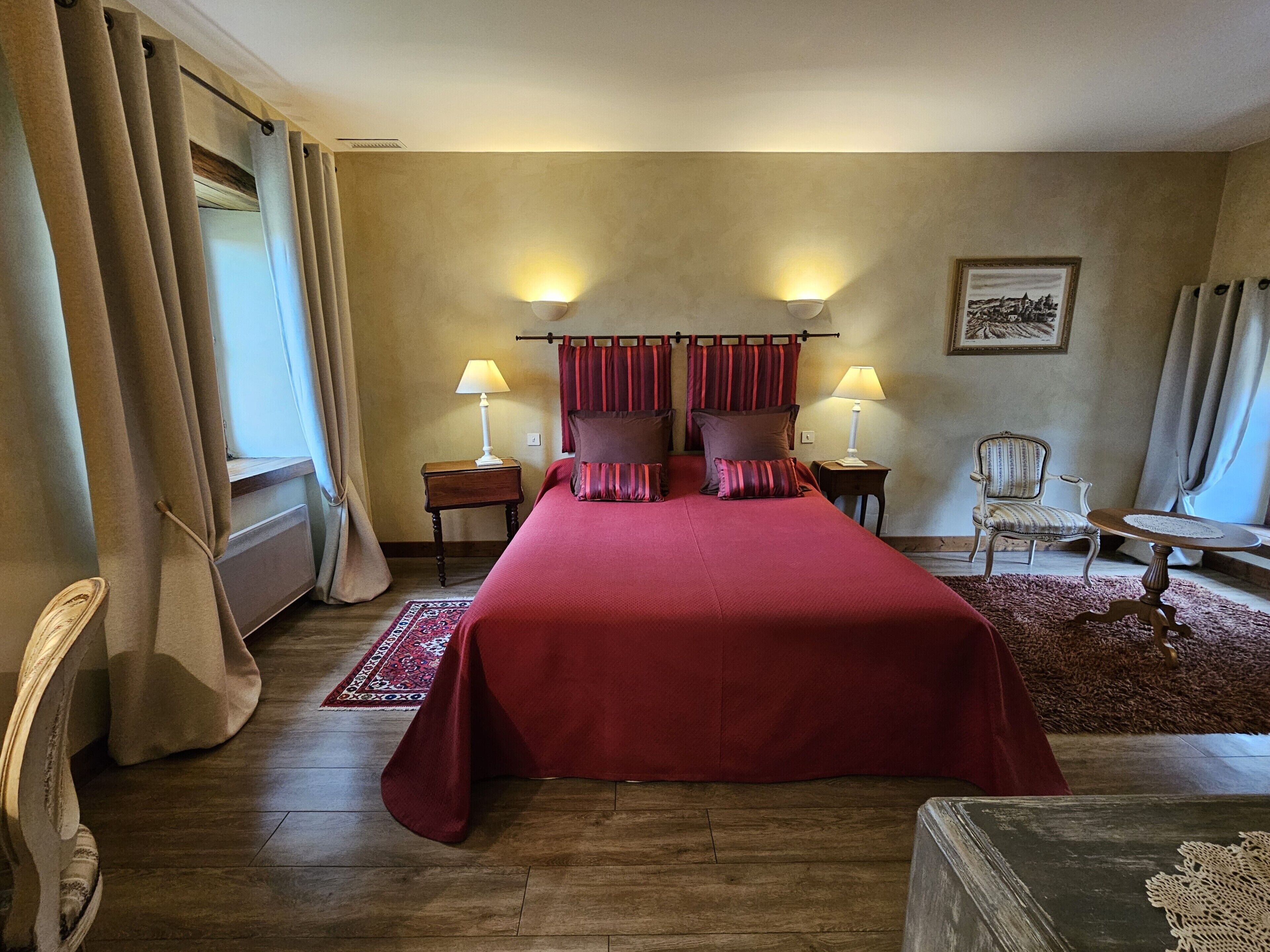 A hotel room with a large bed, two bedside tables with lamps, a chair, a small table, and a rug.