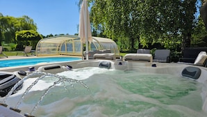 Un jacuzzi con chorros de agua, rodeado de mobiliario exterior y un invernadero.
