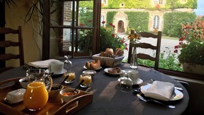 Mesa de comedor con desayuno, un jarrón de flores y vista a un edificio con muros cubiertos de hiedra.