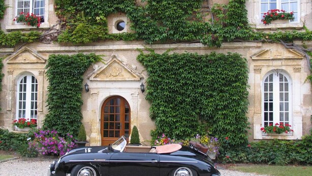 Un clásico descapotable negro estacionado frente a un edificio histórico con muros cubiertos de hiedra y jardineras.