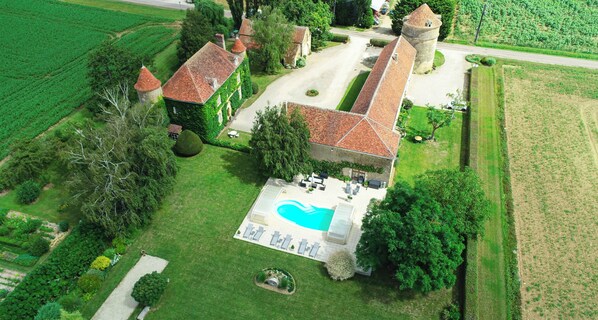 An aerial view of a property with a swimming pool, a tennis court, and a tower.