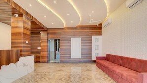 Un vestíbulo moderno con suelo de mármol, paneles de madera, un sofá rojo y una puerta de cristal que da a otra zona.