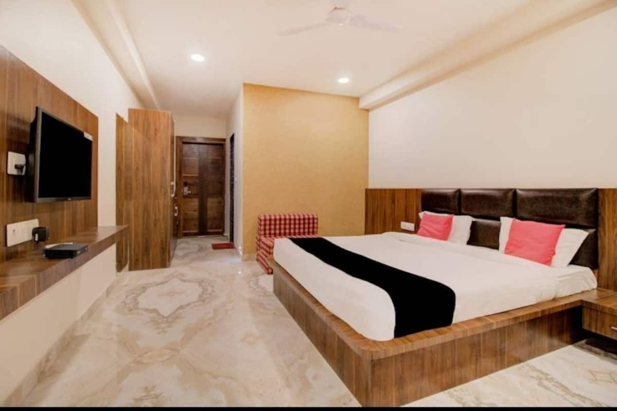Une chambre d’hôtel avec un lit, une télévision, une tête de lit en bois et un banc à carreaux.