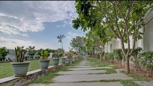 Un sendero bordeado de plantas en macetas y árboles, que conduce a un edificio con arcos al fondo.