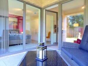 Un intérieur moderne avec une porte vitrée donnant sur une chambre, un coin salon avec un canapé et une petite table agrémentée d’un objet décoratif.