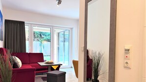 A modern living room with a red sofa, a small table, and a grey ottoman. There is a large mirror on the wall and a potted plant. - Relaxing vacation at its finest in the Strandgut apartment. (Dangast)