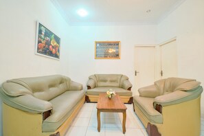 A living room with two beige sofas, a wooden coffee table, and a framed picture on the wall. - Hotel O Brosta (Yogyakarta)