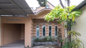 Une maison avec un porche, un petit jardin agrémenté de plantes en pot et un arbre aux fleurs jaunes.