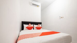 Une chambre d’hôtel avec un lit, des murs blancs et une tête de lit noire.